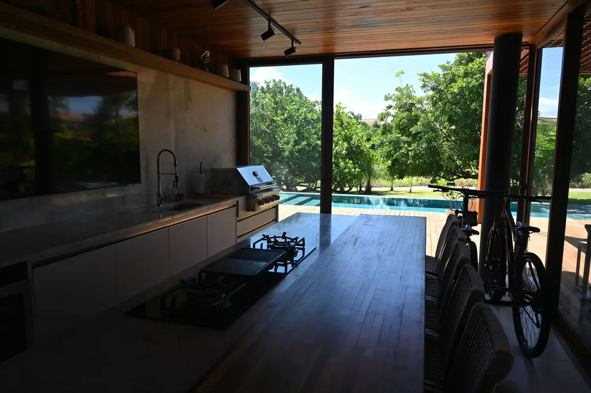 Área gourmet com TV, cooktop e a piscina ao fundo