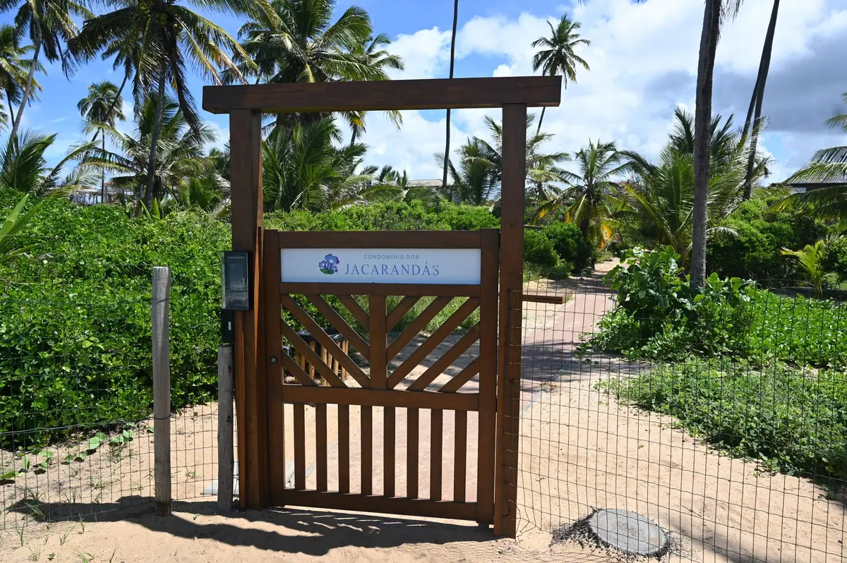 Portão de madeira do Jacarandás no caminho de areia entre coqueiros
