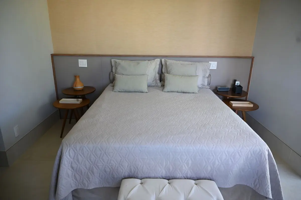 Suíte clara com cama de casal e banco capitonê